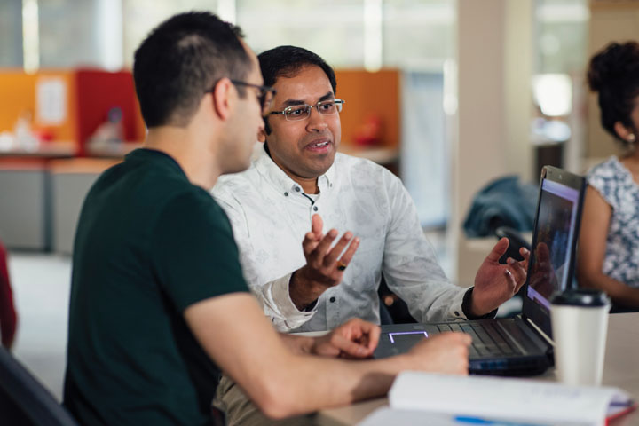 Man gesturing with colleague in front of a laptop