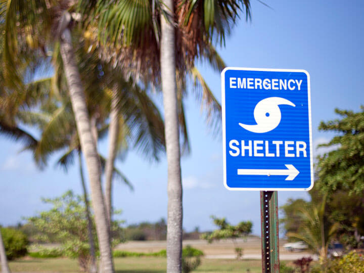 Storm Shelters Testing and Certification with blue "Emergency Shelter" sign and palm trees in the background